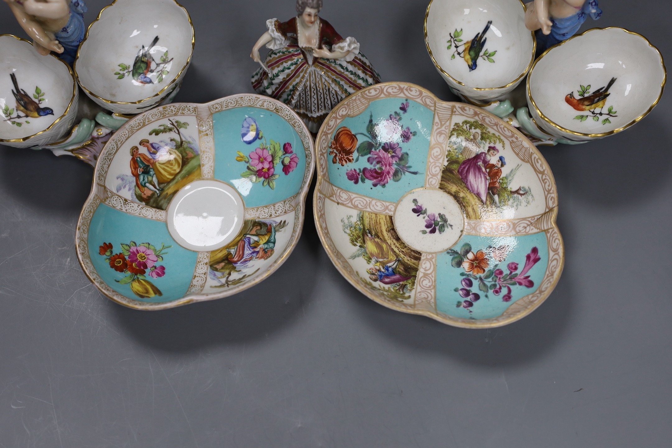 Two Berlin figural salts, 13cm high together with two Dresden saucers and a continental figurine
